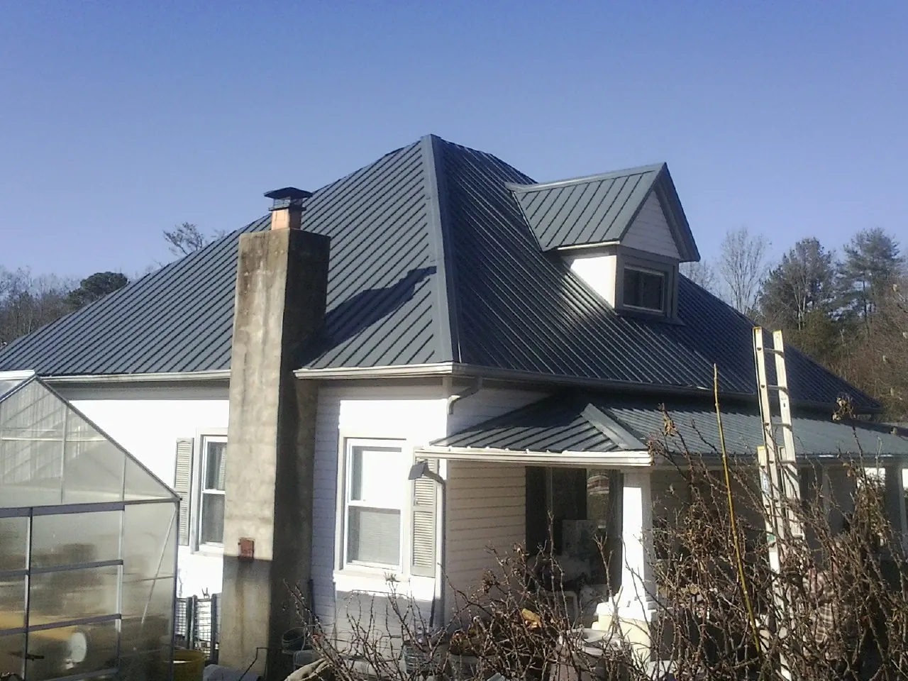 Dark blue standing seam metal roof on a white farmhouse with dormer — Slate & Tile Roof Repair by Roofing Brothers in Ashburn