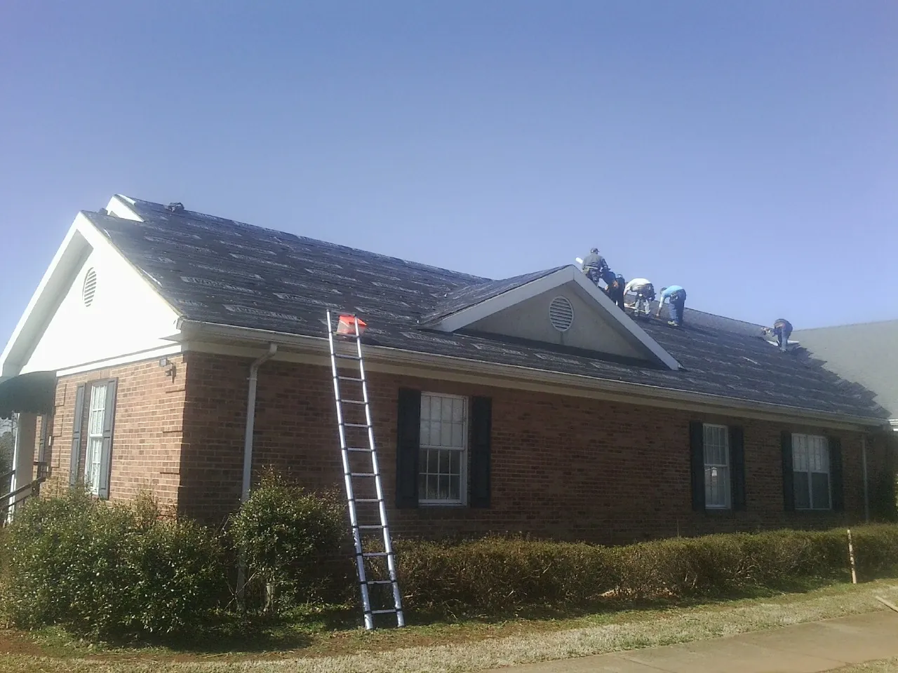 Crew tearing shingles off a brick ranch roof with a ladder set — Metal Roof Repair work by our crew in Ashburn