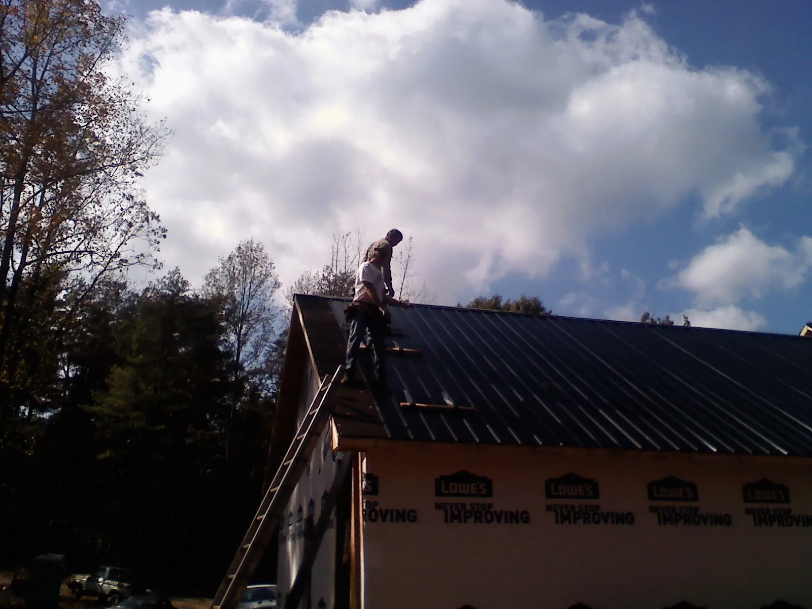Roofer fastening dark metal panels high against a cloudy sky, from a Roof Inspection job in Ashburn